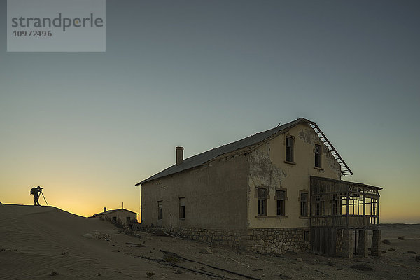 Eine Person macht Fotos von den verlassenen Häusern in der Namib-Wüste bei Sonnenuntergang; Kolmanskop  Namibia'.