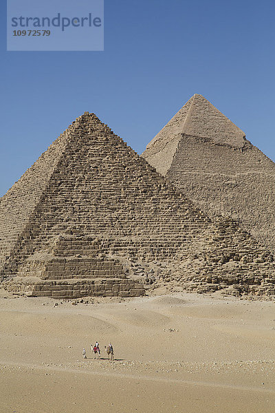 Kamele mit Tourist und Führer  Pyramide der Königin und Chephren-Pyramide (Hintergrund)  Die Pyramiden von Gizeh; Gizeh  Ägypten'.