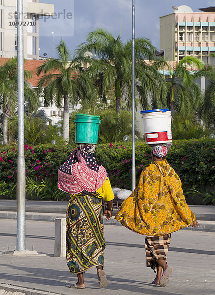 Frauen  die mit großen Plastikeimern auf dem Kopf die Straße entlanggehen; Dar es Salaam  Tansania