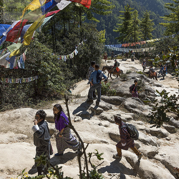 Menschen zu Fuß und auf Pferden auf dem Taktsang-Pfad  über dem Gebetsfahnen hängen; Paro  Bhutan'.