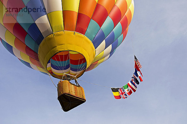Blick nach oben unter einen bunten Heißluftballon  der mit einer multinationalen Flagge im Schlepptau davonschwebt; Ripon  Kalifornien  Vereinigte Staaten von Amerika'.
