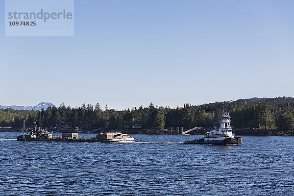 Ein Schlepper zieht an einem klaren Tag in den Tongass Narrows  Ketchikan  Südost-Alaska  USA  Frühjahr  einen Lastkahn aus dem Hafen ins Meer.