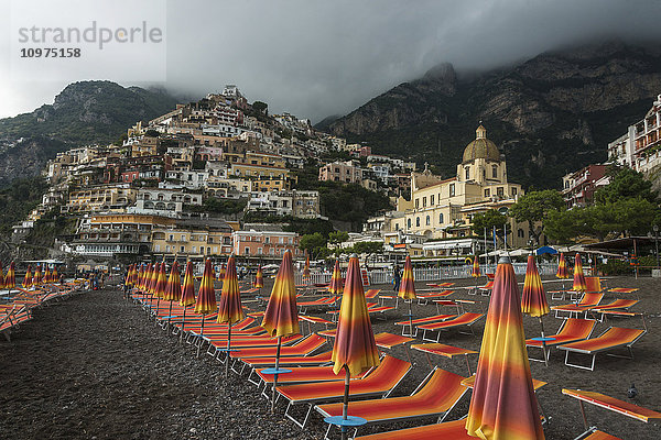 Bunte Liegestühle am Strand mit Häusern auf einem Hügel entlang der Amalfiküste; Positano  Kampanien  Italien'.