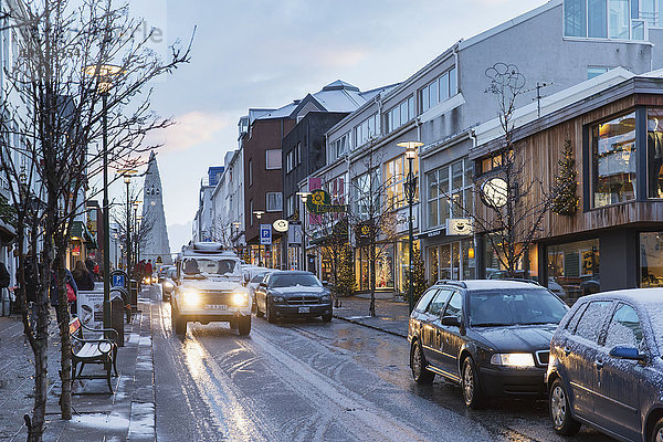 Autos auf der Straße Laugavegur im Zentrum Reykjaviks während der Dämmerung im Winter  im Hintergrund die Hallgrimskirkja; Reykjavik  Island'.