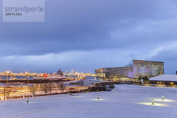 Die öffentliche Konzerthalle Harpa vom Arnarholl-Park aus gesehen  entworfen vom dänischen Büro Henning Larsen Architects und dem isländischen Büro Batteriao Architects  die Glasfassade wurde vom isländischen Glaskünstler Olafur Eliasson entworfen  ein Schneefeld im Vordergrund in der Dämmerung; Reykjavik  Island'