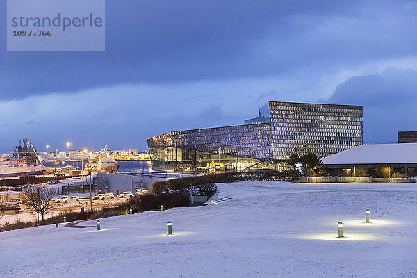 Die öffentliche Konzerthalle Harpa vom Arnarholl-Park aus gesehen  entworfen vom dänischen Büro Henning Larsen Architects und dem isländischen Büro Batteriao Architects  die Glasfassade wurde vom isländischen Glaskünstler Olafur Eliasson entworfen  ein Schneefeld im Vordergrund in der Dämmerung; Reykjavik  Island'