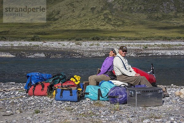 Flößer sitzen auf einem Stapel Ausrüstung in der Sonne entlang des Canning River im Arctic National Wildlife Refuge  Sommer  Alaska