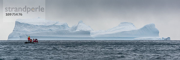Schlauchboot steuert auf blauen Eisberg am Horizont zu; Antarktis