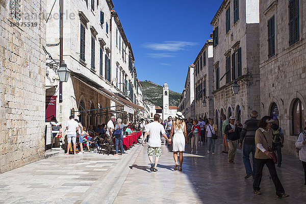 Menschen  die zwischen Gebäuden und Restauranttischen im Freien in der Altstadt von Dubrovnik spazieren gehen; Dubrovnik  Kroatien'.