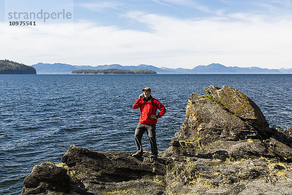 Mann telefoniert mit einem Handy auf einer Klippe oberhalb der Tongass Narrows in der Nähe von Ketchikan  Südost-Alaska  Frühling