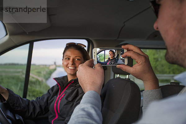 Ein Mann fotografiert eine junge Frau mit einem Smartphone  während er in einem Fahrzeug sitzt; Egmond aan Zee  Holland'.