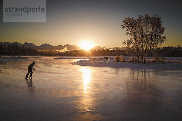 Ein Schlittschuhläufer läuft Schlittschuh auf der Westchester Lagoon bei Sonnenaufgang in der Innenstadt von Anchorage  Süd-Zentral-Alaska  Winter