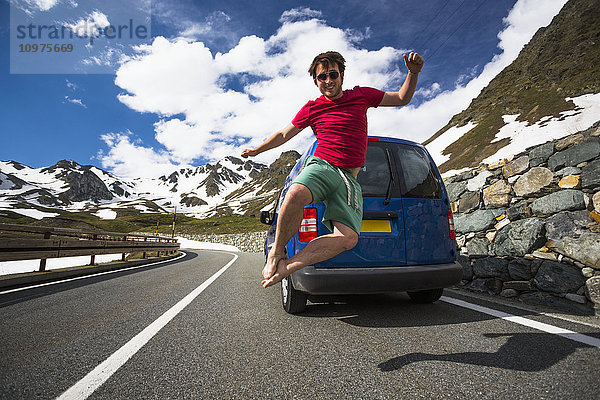 Ein junger Mann springt auf einer Passstraße in den Westalpen in die Luft; Italien'.