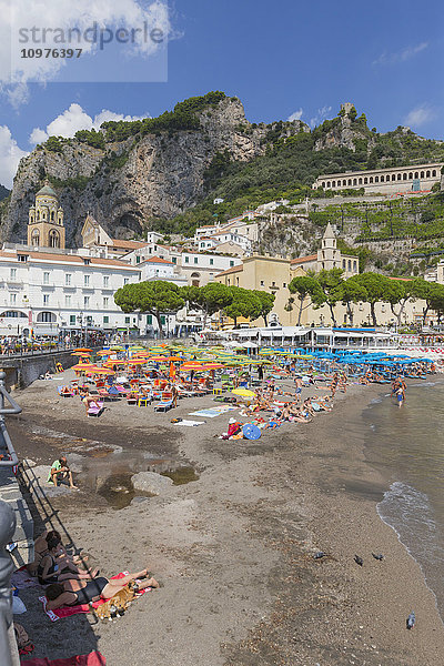 Strandansicht der Stadt Amalfi an der Amalfiküste in Italien  mit am Strand liegenden Touristen und den Dorfgebäuden und Bergen im Hintergrund; Amalfi  Provinz Salerno  Italien'.