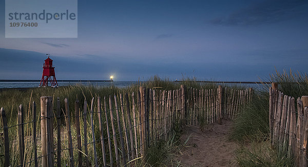 Ein mit einem Holzzaun gesäumter Sandweg führt zum Strand mit dem Leuchtturm Herd Groyne am Ufer; South Shields  Tyne and Wear  England'.