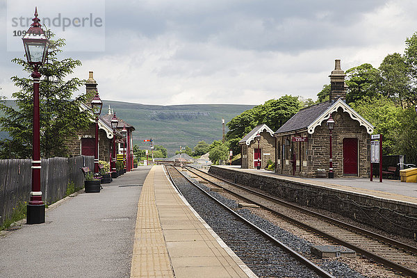 Kleines steinernes Bahnhofsgebäude mit roten Laternenpfählen entlang der Bahngleise; Garsdale  Yorkshire  England
