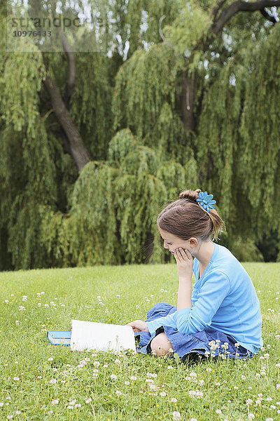 Mädchen sitzt im Park und liest ein Buch; Toronto  Ontario  Kanada'.