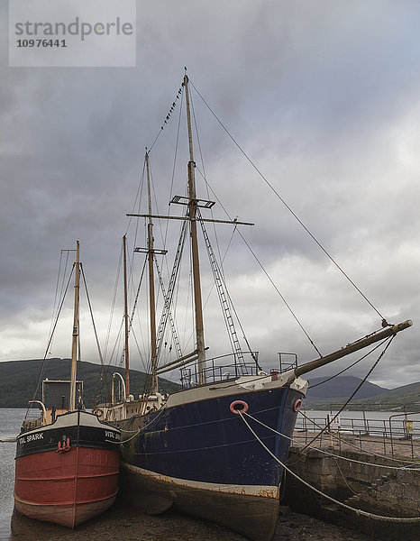 Große Segelboote mit Masten  die an einem Pier unter bewölktem Himmel festmachen; Schottland'.