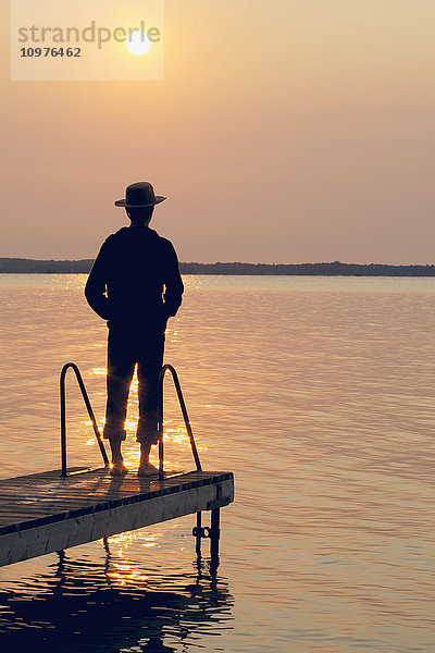Mann am Ende des Stegs bei Sonnenaufgang am Balsam Lake; Ontario  Kanada'.