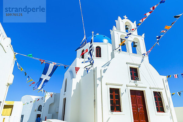 Eine traditionelle griechisch-orthodoxe Kirche mit Weltflaggen  die in allen Richtungen zur Feier des Tages wehen  und der griechischen Flagge; Oia  Santorin  Griechenland'