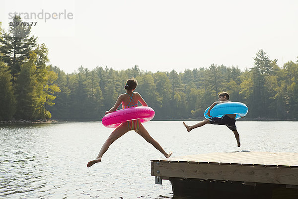 Kinder springen vom Ende eines Stegs mit aufblasbaren Ringen am Crystal Lake; Ontario  Kanada'.