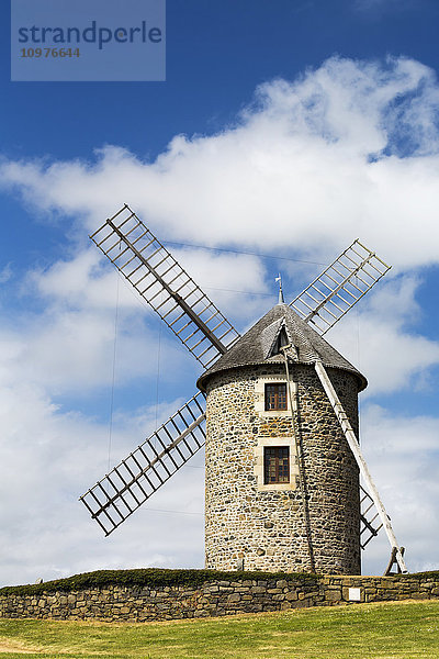 Eine alte Steinwindmühle auf einem Hügel mit hölzernen Flügeln  umgeben von einem Steinzaun mit blauem Himmel und Wolken; Brehec  Bretagne  Frankreich'.