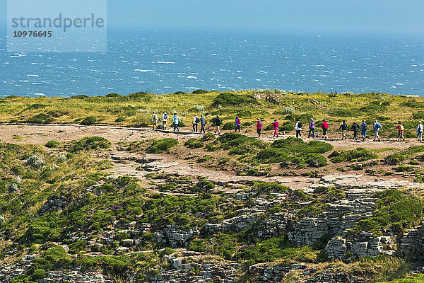 Mehrere Spaziergänger auf einem Steinweg mit Blick auf das Meer und den blauen Himmel; Frehal  Bretagne  Frankreich'.