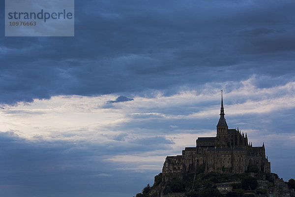 Silhouette einer großen Steinabtei auf einem felsigen Hügel mit dramatischen Wolken bei Sonnenuntergang; Mont St. Michel  Bretagne  Frankreich'.