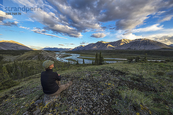 Frau sitzt auf einem Felsen und schaut auf den Wind River im Peel Watershed; Yukon  Kanada'.