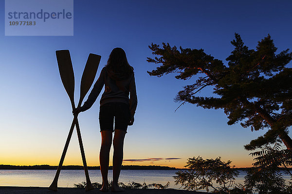 Mädchen hält Paddel mit Blick auf den Balsam Lake bei Sonnenaufgang; Ontario  Kanada'.