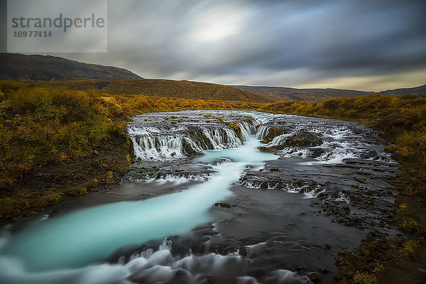 Langzeitbelichtung von über Felsen fließendem Wasser in einem Bach und dunklen Wolken am Himmel; Bruarfoss  Island'.