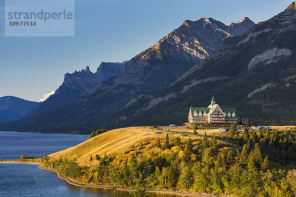 Prince of Wales Hotel auf einer Bergkuppe bei Sonnenaufgang mit Blick auf einen See mit Bergen im Hintergrund und blauem Himmel; Waterton  Alberta  Kanada'.