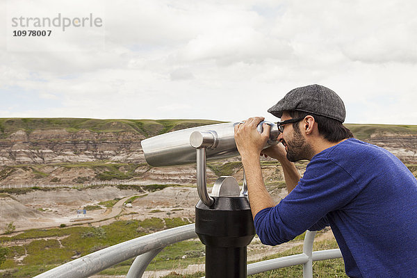 Mann  der im Royal Tyrell Museum Of Palaeontology im Freien durch ein Fernglas schaut; Drumheller  Alberta  Kanada'.