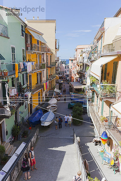 Blick auf die Wohnhäuser  deren Balkone mit Kleidern geschmückt sind  und auf die Geschäfte und Touristen in den Straßen von Manarola; Manarola  Ligurien  Italien'.