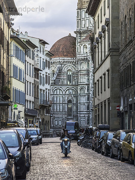 Ein Motorradfahrer auf einer Kopfsteinpflasterstraße mit der Kathedrale von Florenz im Hintergrund; Florenz  Italien