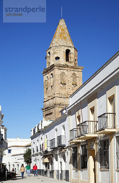 Fußgänger gehen eine Straße neben einem Wohnhaus und einem Turm entlang; Medina Sidonia de la Frontera  Andalusien  Spanien'.