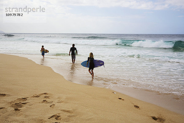 Drei junge Surfer gehen am Strand entlang  Pipeline; Oahu  Hawaii  Vereinigte Staaten von Amerika'.