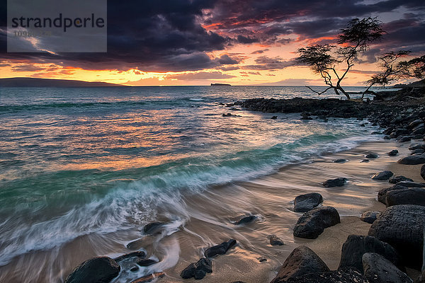 Ein dramatischer Himmel bei Sonnenuntergang über einem türkisfarbenen Meer entlang der Küste einer hawaiianischen Insel; Hawaii  Vereinigte Staaten von Amerika'.
