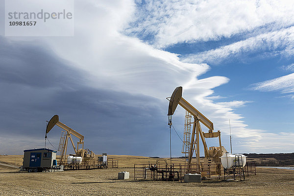 Zwei Pumpjacks mit Gewitterwolken in der Ferne und etwas blauem Himmel; Alberta  Kanada'.