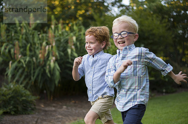 Zwei Jungen mit einem breiten Lächeln  die zusammen auf einer Wiese laufen; Raleigh  North Carolina  Vereinigte Staaten von Amerika