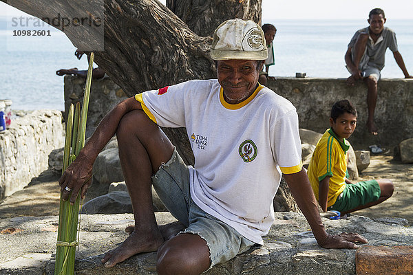 Mann sitzt auf einem Steinvorsprung am Strand; Manatuto  Osttimor