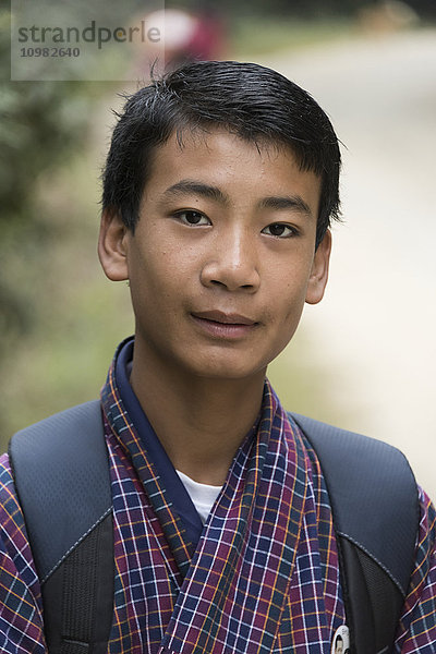 Porträt eines Jungen mit kariertem Gewand  der einen Rucksack trägt; Punakha  Bhutan