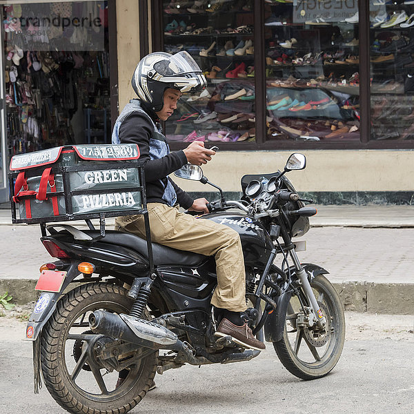 Pizzabote auf einem Motorrad auf der Straße mit einem Smartphone; Thimphu  Bhutan