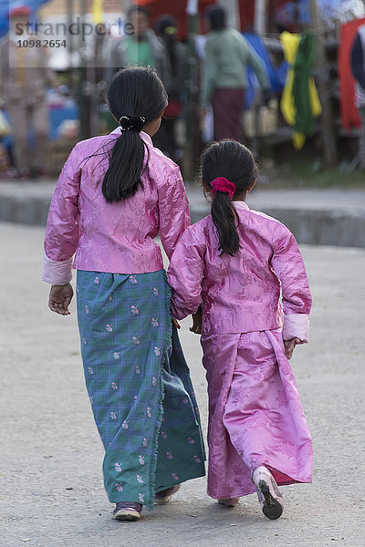 Zwei junge Mädchen in traditioneller Kleidung gehen gemeinsam eine Straße entlang; Paro  Bhutan'.