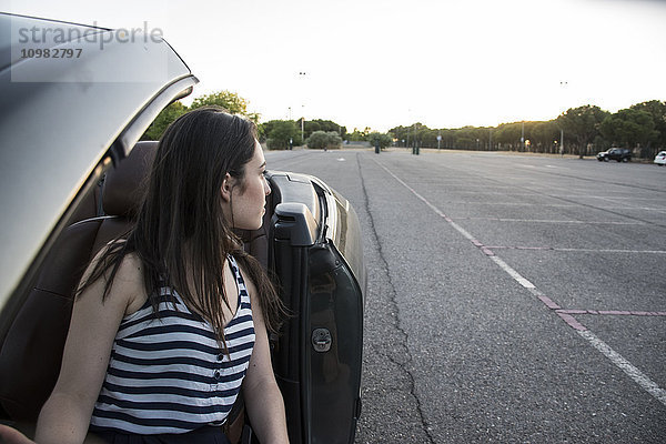 Junge Frau sitzt im Cabrio und schaut sich etwas an.