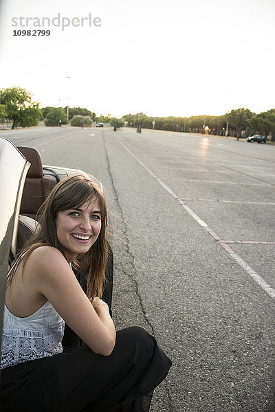 Lächelnde junge Frau kauernd neben dem Cabriolet