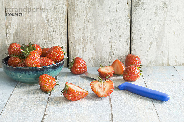 Schale mit Erdbeeren und Küchenmesser auf Holz