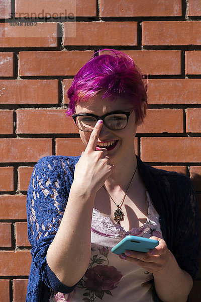 Porträt einer lachenden jungen Frau mit gefärbtem Haar  die ihre Brille anpasst.