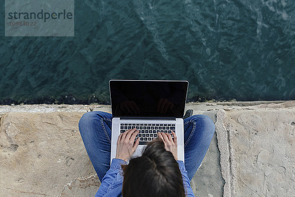 Junge Frau sitzend auf dem Dock mit Laptop