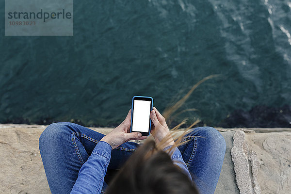 Junge Frau sitzt auf dem Dock mit dem Handy